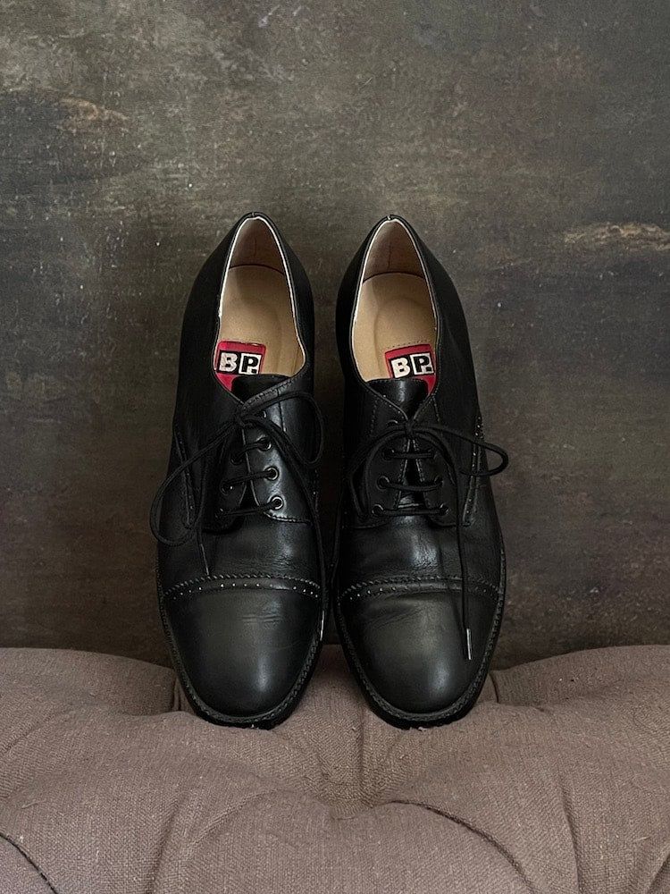 Vintage 90s y2k historically inspired black leather oxford heels with lace up detail, in front of historical painting background.