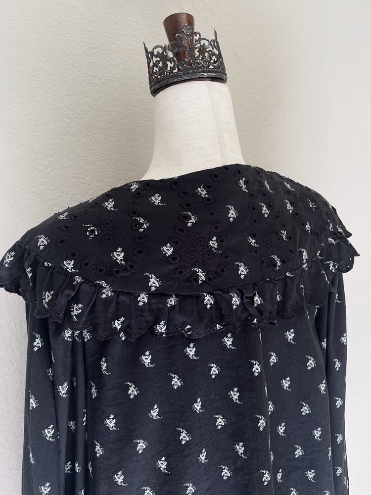 A black floral print historically inspired baroque blouse with large lace trimmed collar and long bishop sleeves is pictured on a mannequin from the back