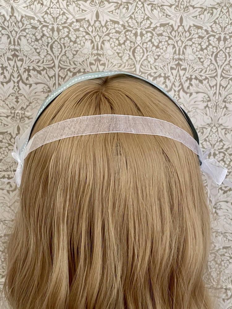 A Handmade historically inspired regency era ribbon headdress in sage green with bow accents on a mannequin.