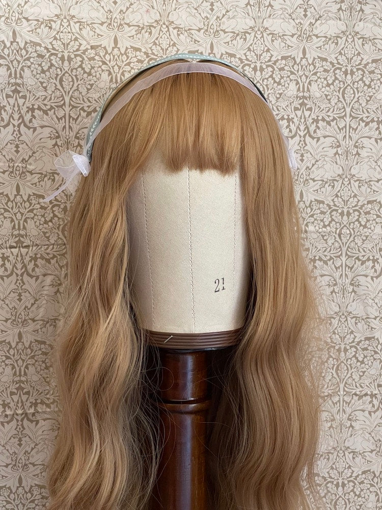 A Handmade historically inspired regency era ribbon headdress in sage green with bow accents on a mannequin.