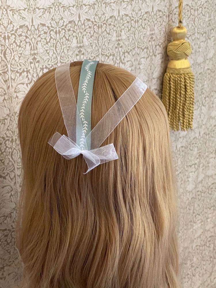 A Handmade historically inspired regency era ribbon headdress in sage green with bow accents on a mannequin.