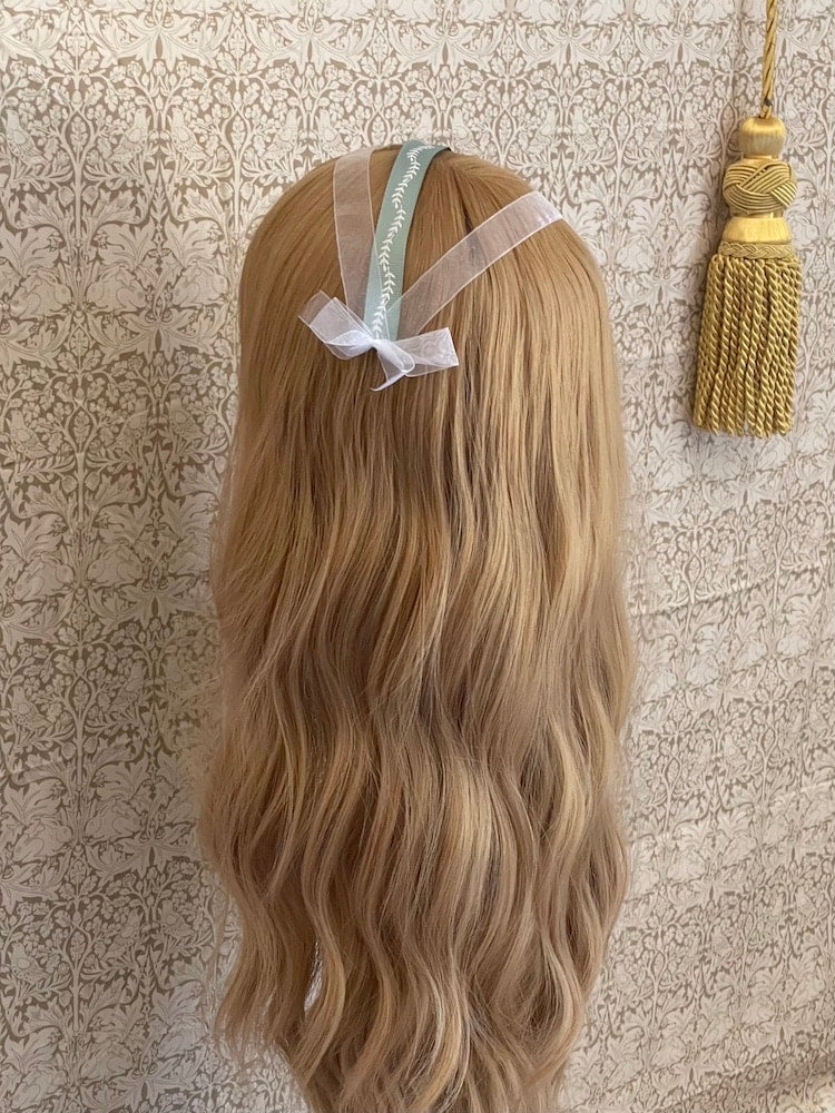 A Handmade historically inspired regency era ribbon headdress in sage green with bow accents on a mannequin.