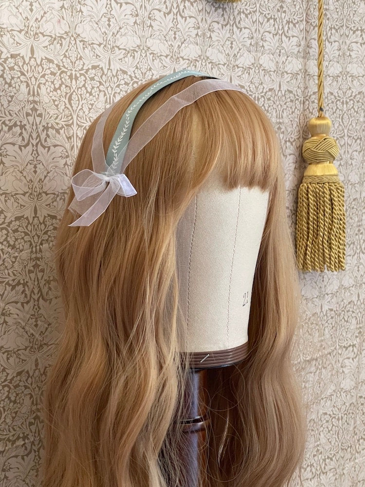 A Handmade historically inspired regency era ribbon headdress in sage green with bow accents on a mannequin.