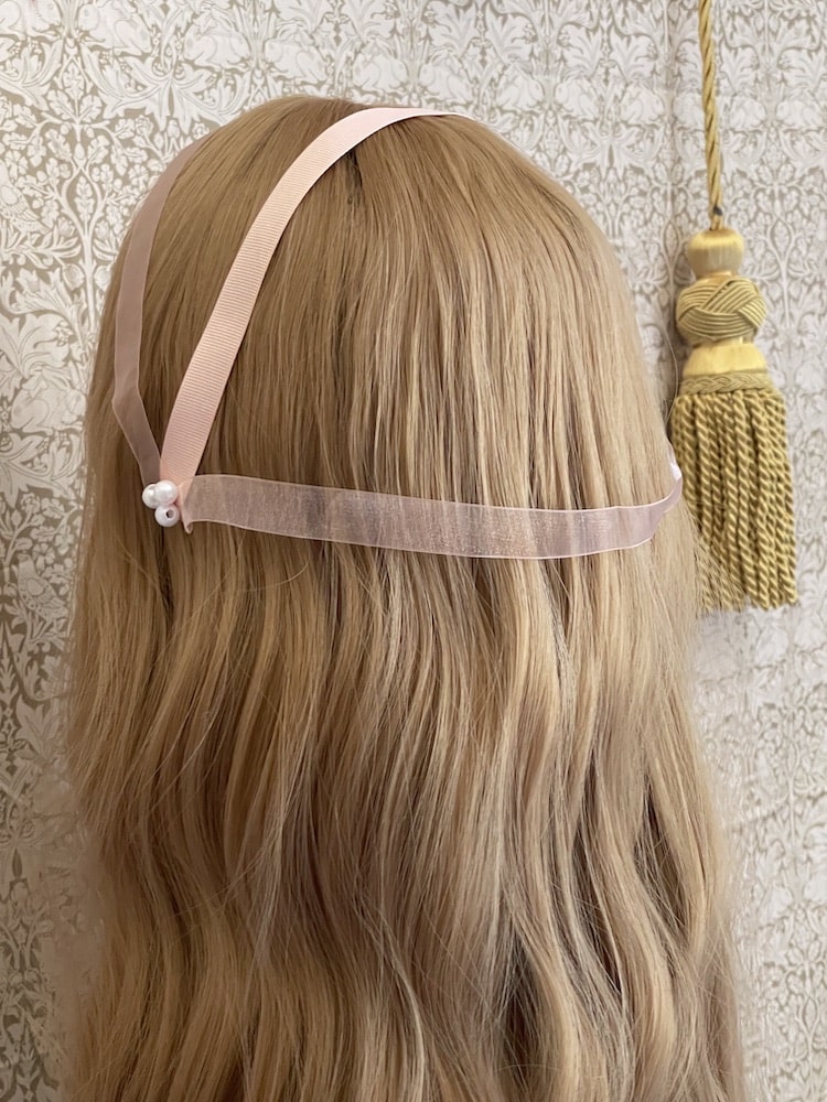 A handmade historically inspired regency era headdress in peachy pink with pearl accent is pictured on a mannequin.