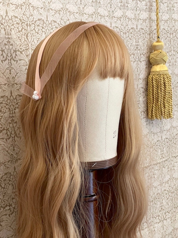 A handmade historically inspired regency era headdress in peachy pink with pearl accent is pictured on a mannequin.