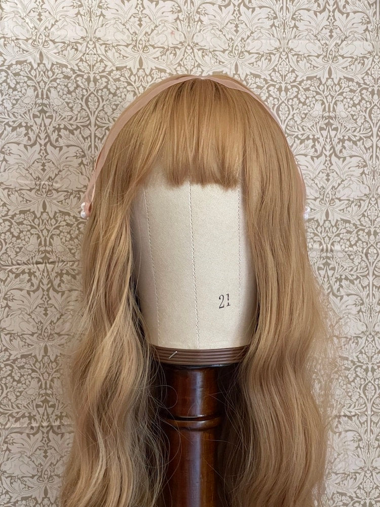 A handmade historically inspired regency era headdress in peachy pink with pearl accent is pictured on a mannequin.