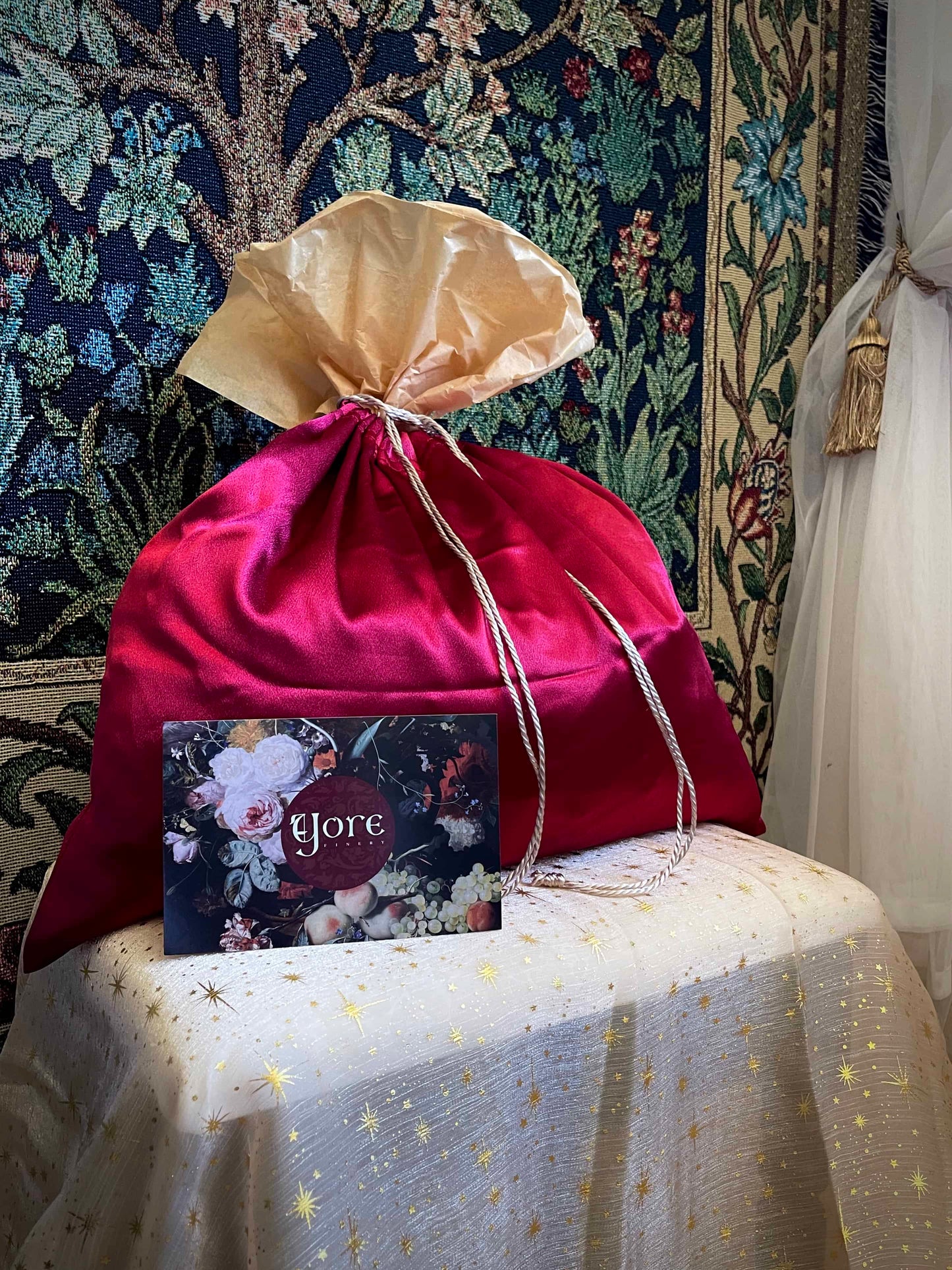 A historical fashion style bundle mystery bag in a satin drawstring bag sits on a celestial puff in front of a historically inspired tapestry.