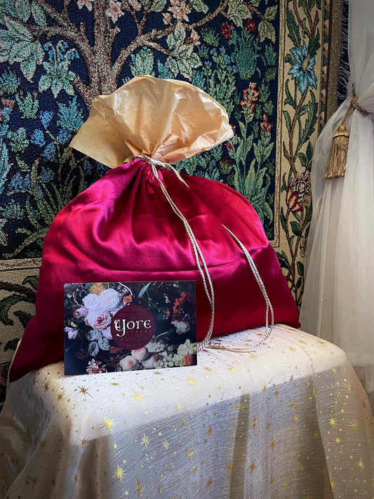 A historical fashion style bundle mystery bag in a satin drawstring bag sits on a celestial puff in front of a historically inspired tapestry.