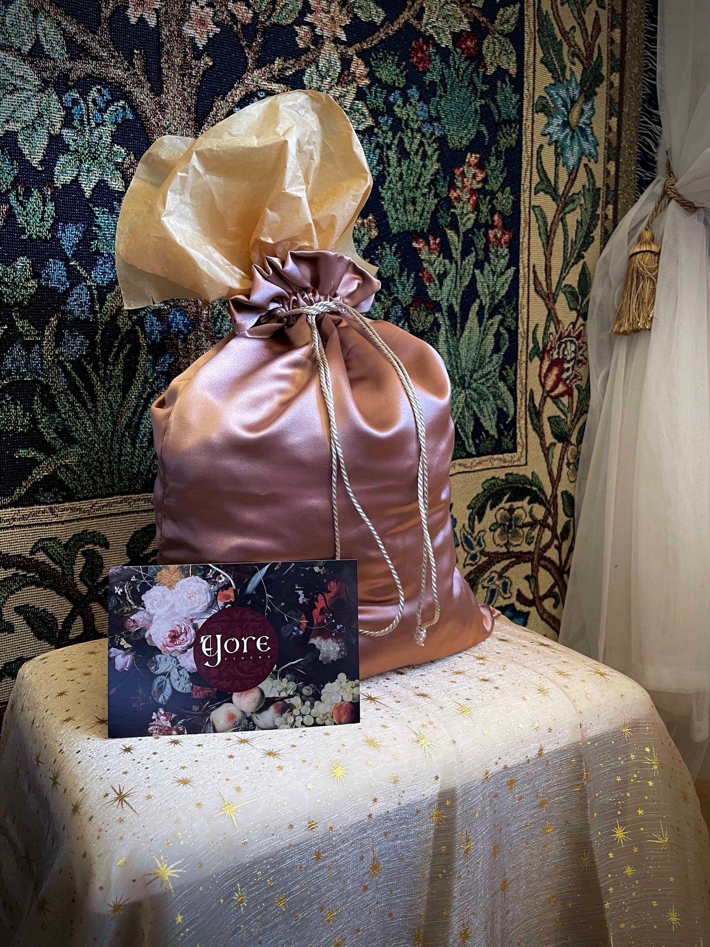 A historical fashion style bundle mystery bag in a satin drawstring bag sits on a celestial puff in front of a historically inspired tapestry.