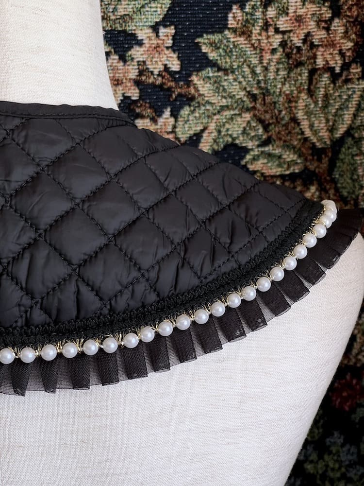 A Historically Inspired Quilted Round Collar with Ruffle & Pearl Trim in Black pictured on a mannequin.