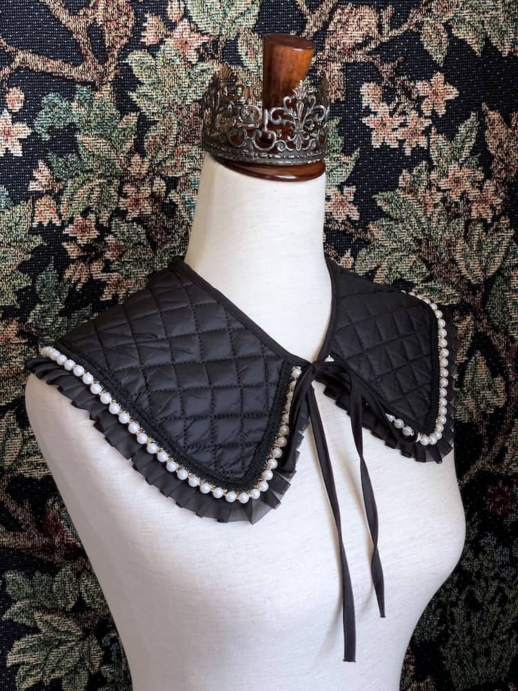A Historically Inspired Quilted Round Collar with Ruffle & Pearl Trim in Black pictured on a mannequin.