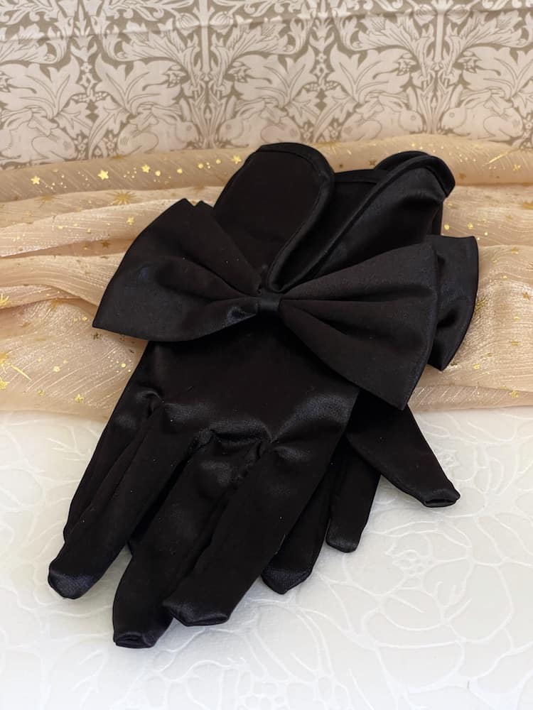 A pair of historically inspired Regency & Victorian era Satin Gloves with Large Bow Detail in Black, pictured on a historical backdrop.