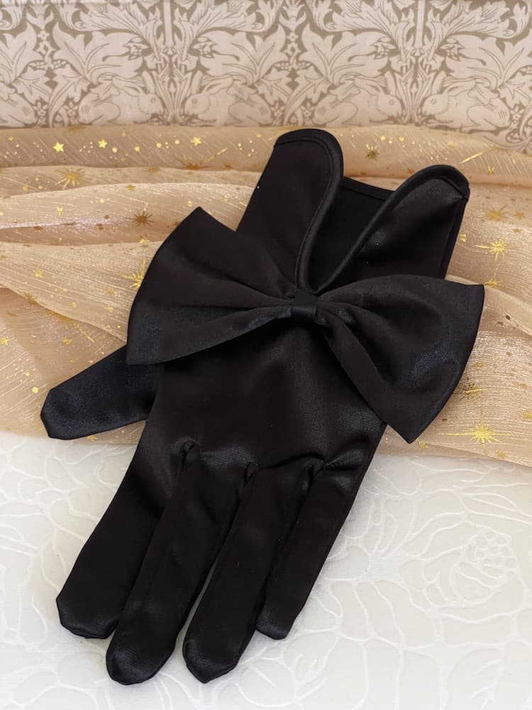 A pair of historically inspired Regency & Victorian era Satin Gloves with Large Bow Detail in Black, pictured on a historical backdrop.