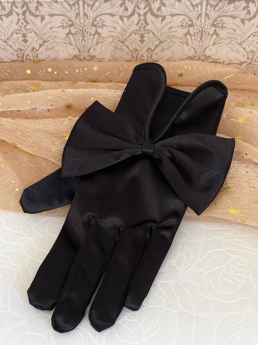 A pair of historically inspired Regency & Victorian era Satin Gloves with Large Bow Detail in Black, pictured on a historical backdrop.