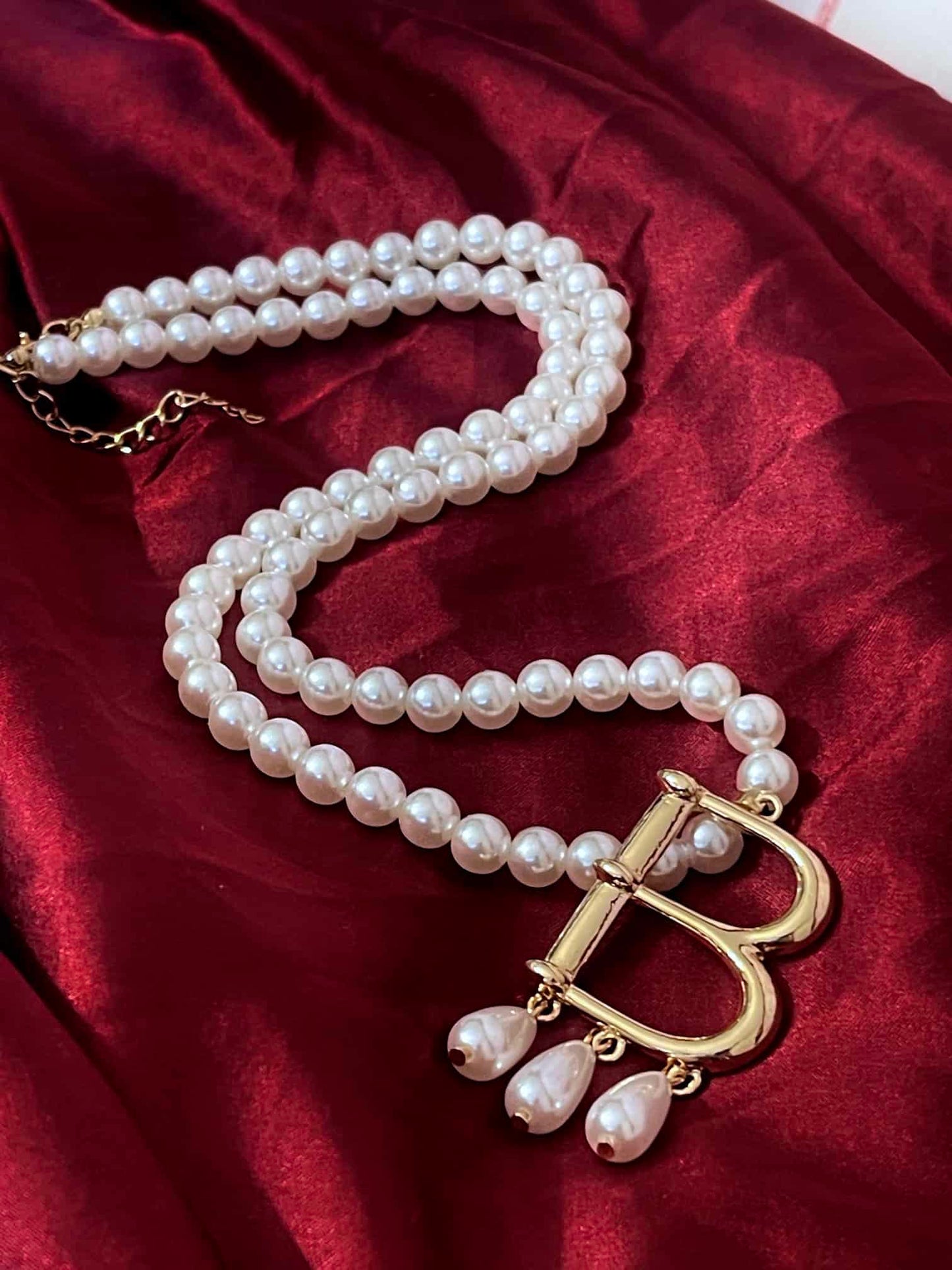 A Historical Tudor Fashion Inspired Anne Boleyn "B" Pearl Necklace on a mannequin in front of an ornate backdrop.