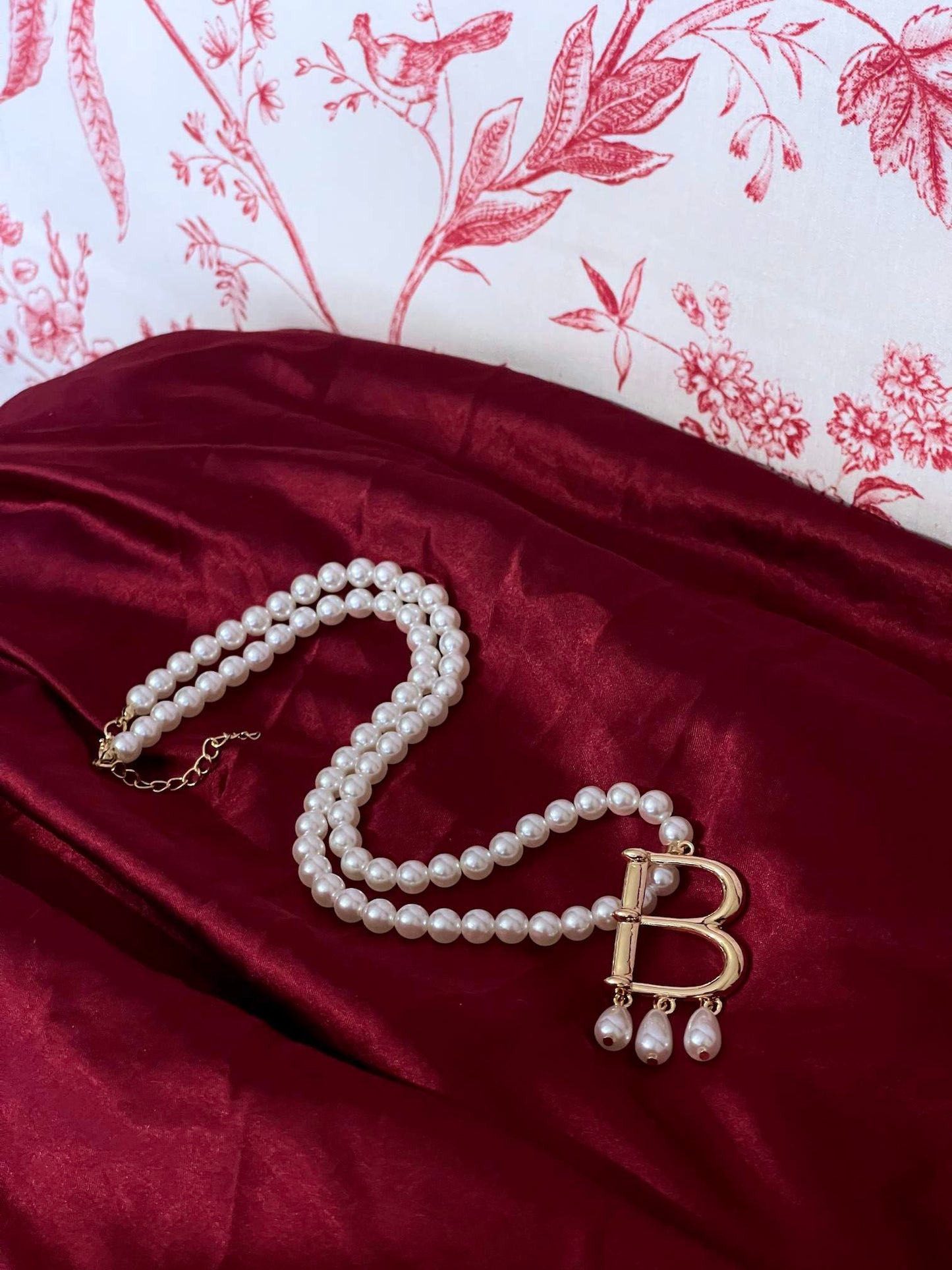 A Historical Tudor Fashion Inspired Anne Boleyn "B" Pearl Necklace on a mannequin in front of an ornate backdrop.