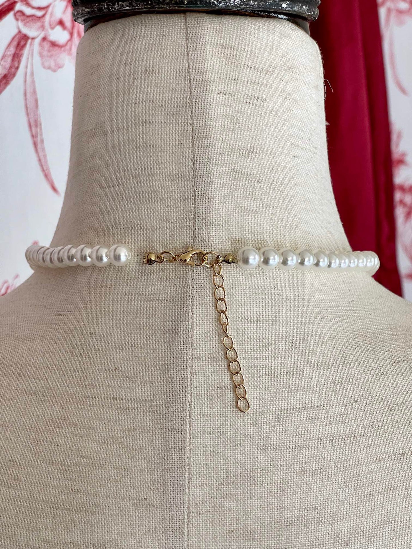 A Historical Tudor Fashion Inspired Anne Boleyn "B" Pearl Necklace on a mannequin in front of an ornate backdrop.