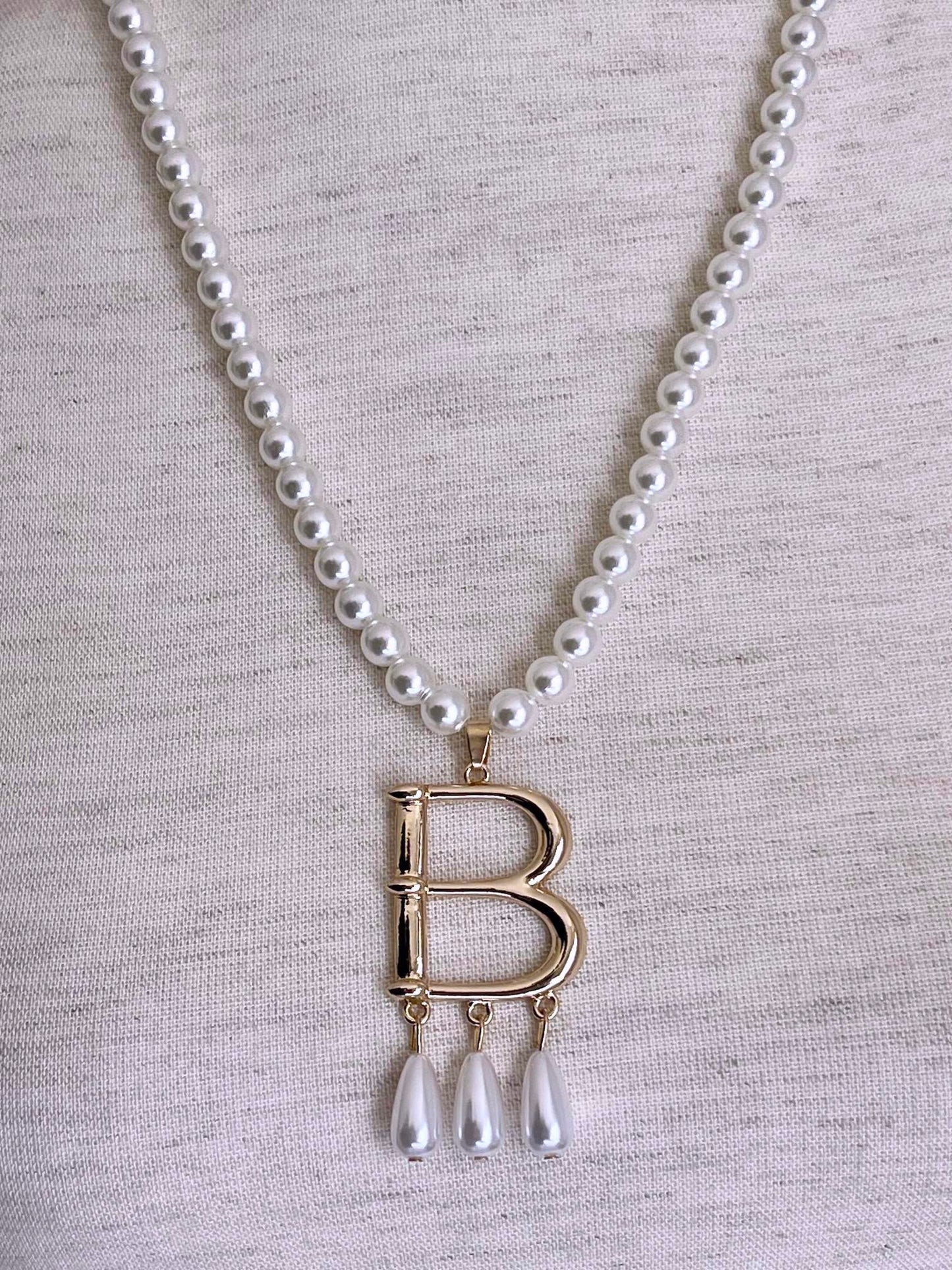 A Historical Tudor Fashion Inspired Anne Boleyn "B" Pearl Necklace on a mannequin in front of an ornate backdrop.