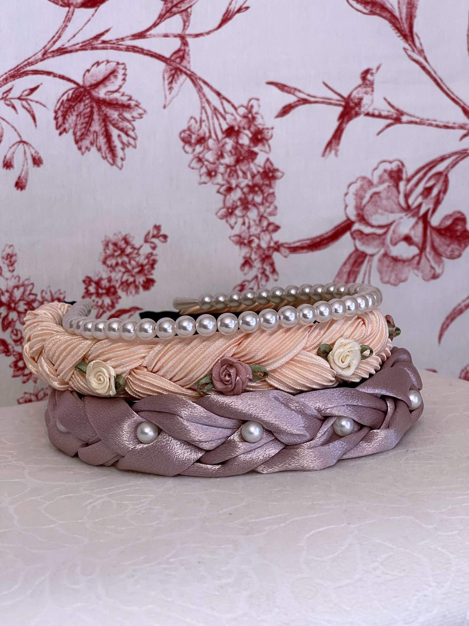 A Historically Inspired Braided Chiffon Rosette Headband in Ballerina Pink with two other pearl satin headbands, perfect for rococo and regency era fashion.