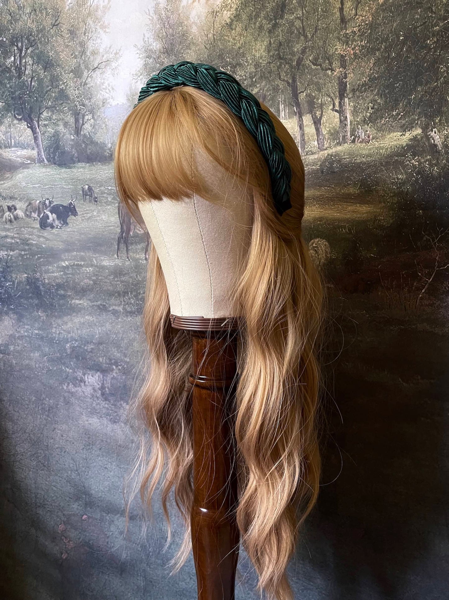 A historically inspired vintage style braided headband in dark forest green is pictured on a mannequin in front of an art history backdrop.
