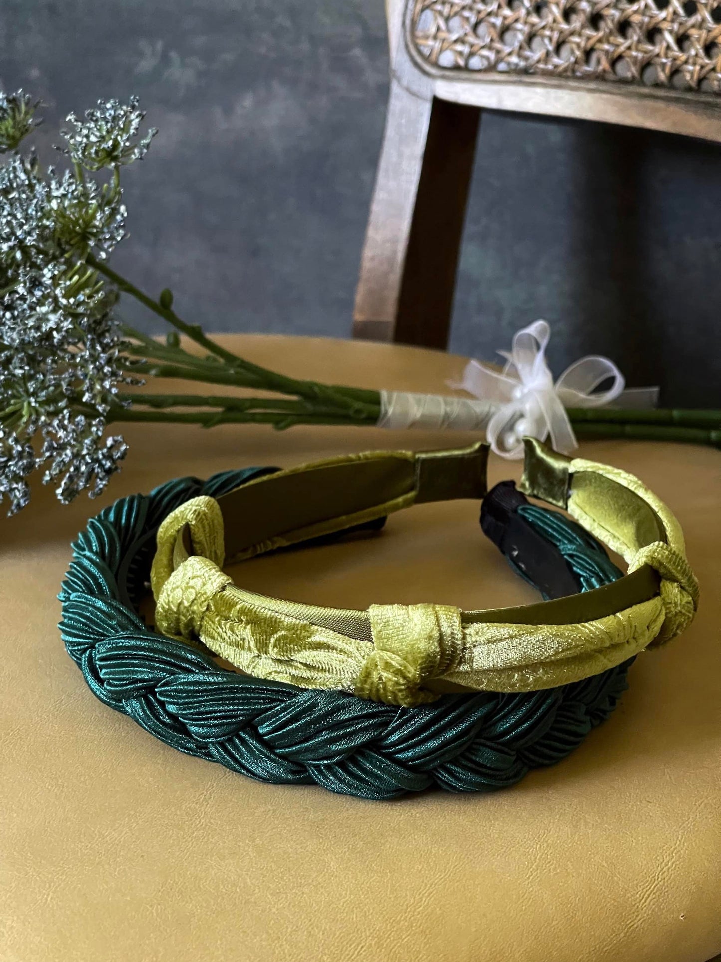 A historically inspired vintage style braided headband in dark forest green is pictured with a floral bouquet in front of an art history backdrop.