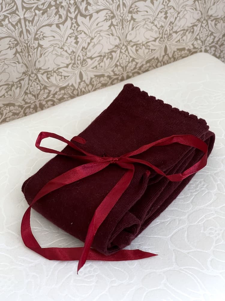 A pair of Historically Inspired Cotton Knee-High Socks with Ribbon Lacing in Burgundy, on a puff. Stockings for any historical era.