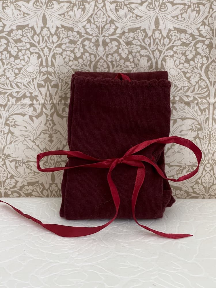 A pair of Historically Inspired Cotton Knee-High Socks with Ribbon Lacing in Burgundy, on a puff. Stockings for any historical era.
