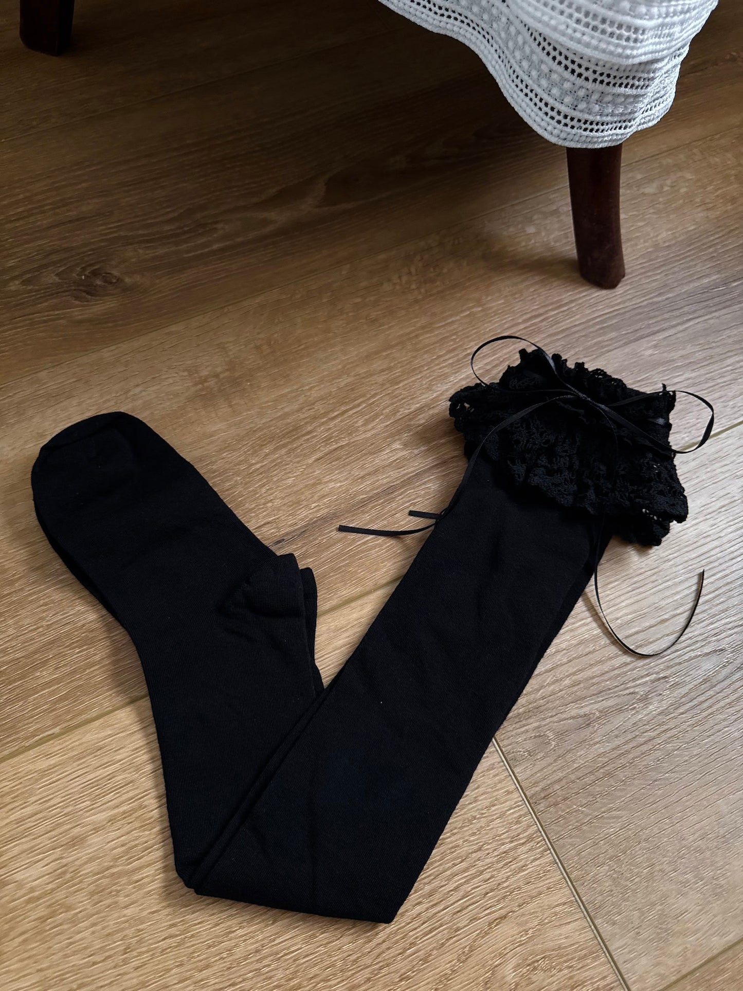 Historically Inspired Cotton Knee-High Socks with ruffled Lace Trim and ribbon ties in gothic Black on a cottagecore wooden floor.