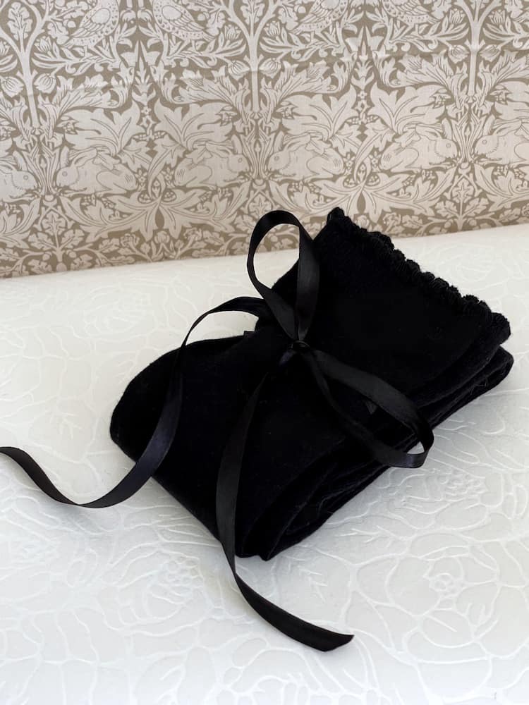 A pair of Historically Inspired Cotton Knee-High Socks with Ribbon Lacing in Black, on a puff. Stockings for any historical era.