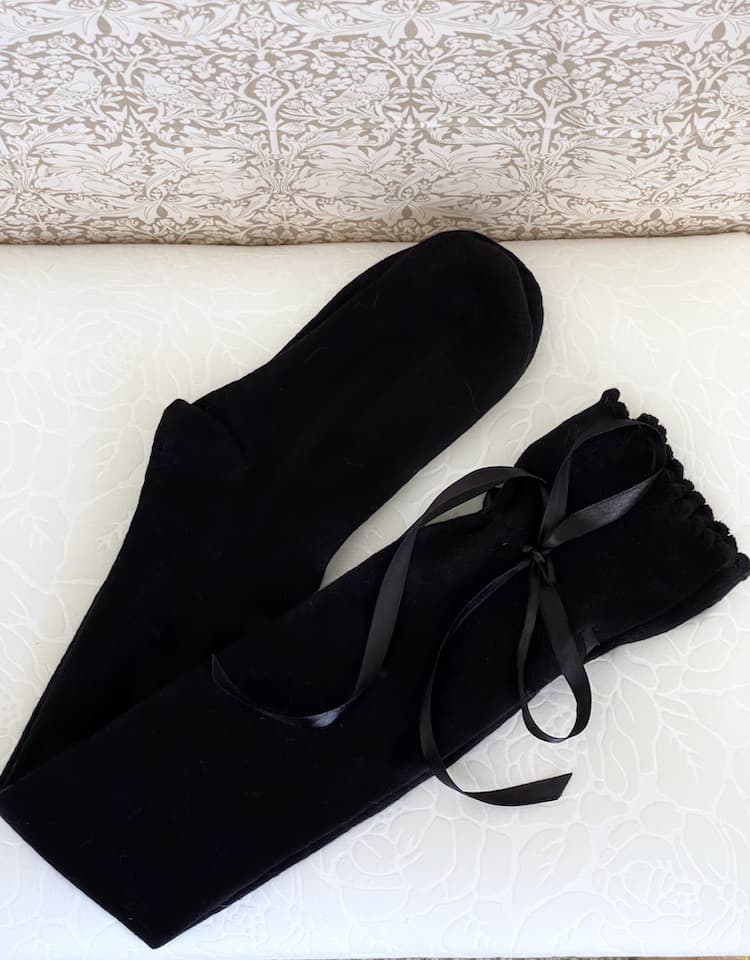 A pair of Historically Inspired Cotton Knee-High Socks with Ribbon Lacing in Black, on a puff. Stockings for any historical era.