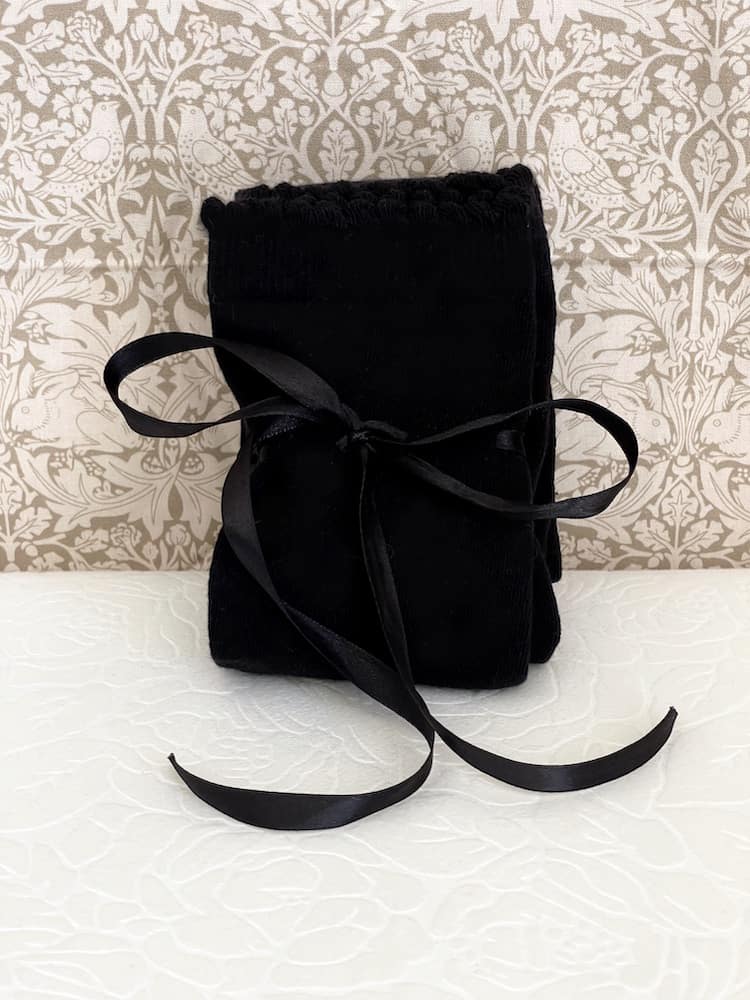 A pair of Historically Inspired Cotton Knee-High Socks with Ribbon Lacing in Black, on a puff. Stockings for any historical era.