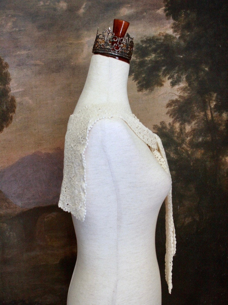Historically Inspired Floral Crochet Folk Shawl / Capelet in Ivory on a mannequin in front of a painting backdrop. Victorian, renaissance, medieval.