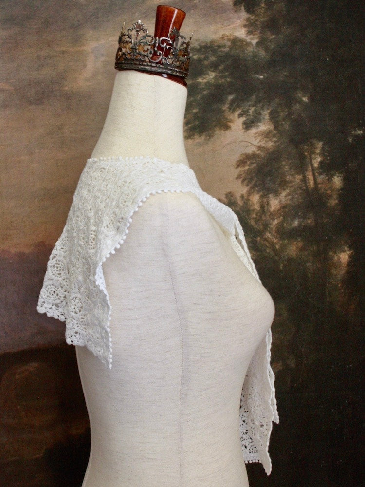 Historically Inspired Floral Crochet Folk Shawl / Capelet in White on a mannequin in front of a painting backdrop. Victorian, renaissance, medieval.