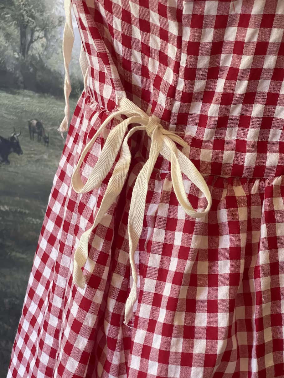 A historically inspired vintage style red and ivory gingham check mini dress with lace trim and ribbon ties.
