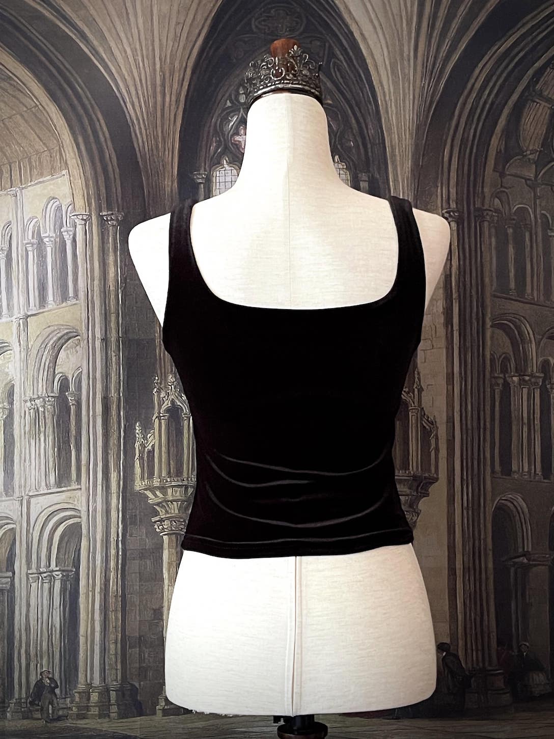 A historically inspired gothic black velvet ruched milkmaid bustier top is pictured on a mannequin in front of a gothic cathedral backdrop.