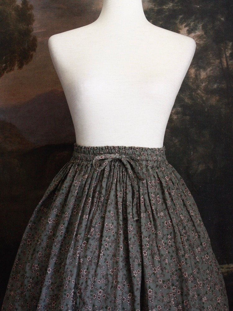 Historically Inspired victorian era peasant turn of the century Printed Floral Cotton Maxi Skirt in Dusty Sage Green pictured on a mannequin in front of a classical painting.