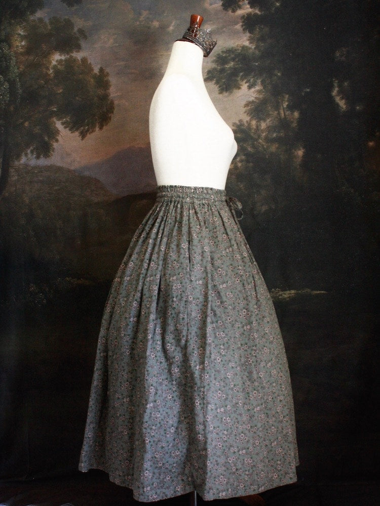 Historically Inspired victorian era peasant turn of the century Printed Floral Cotton Maxi Skirt in Dusty Sage Green pictured on a mannequin in front of a classical painting.