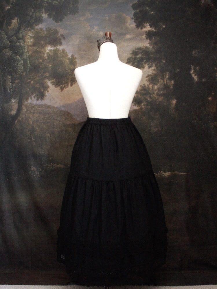 A Historically Inspired bohemian Tiered Cotton Maxi Skirt with floral Lace Trim in Black on a mannequin in front of an art history backdrop.