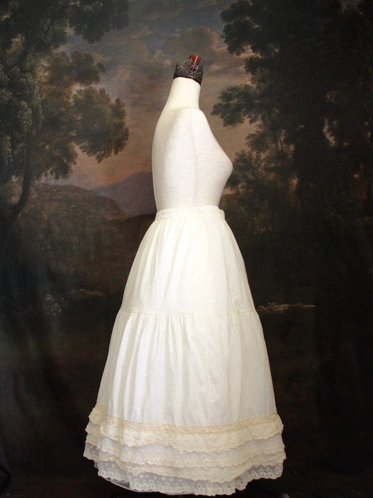 A Historically Inspired bohemian Tiered Cotton Maxi Skirt with floral Lace Trim in Ivory/Cream on a mannequin in front of an art history backdrop.