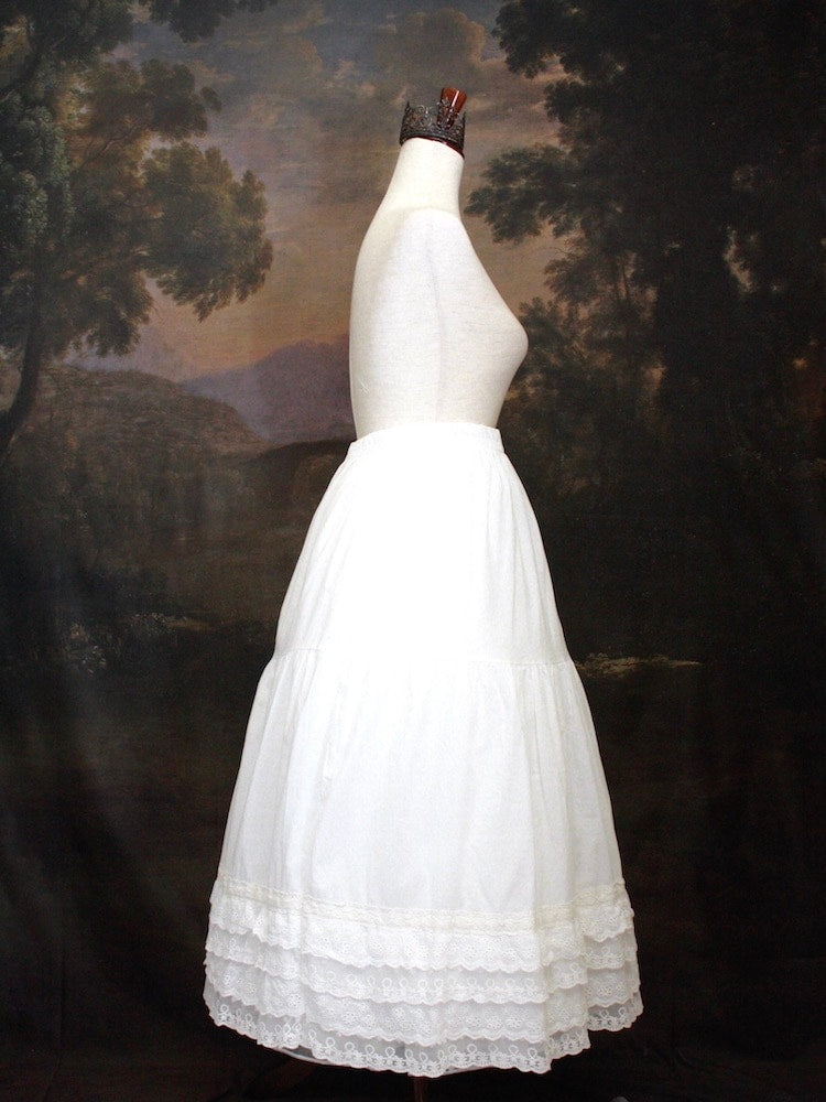A Historically Inspired bohemian Tiered Cotton Maxi Skirt with floral Lace Trim in White on a mannequin in front of an art history backdrop.