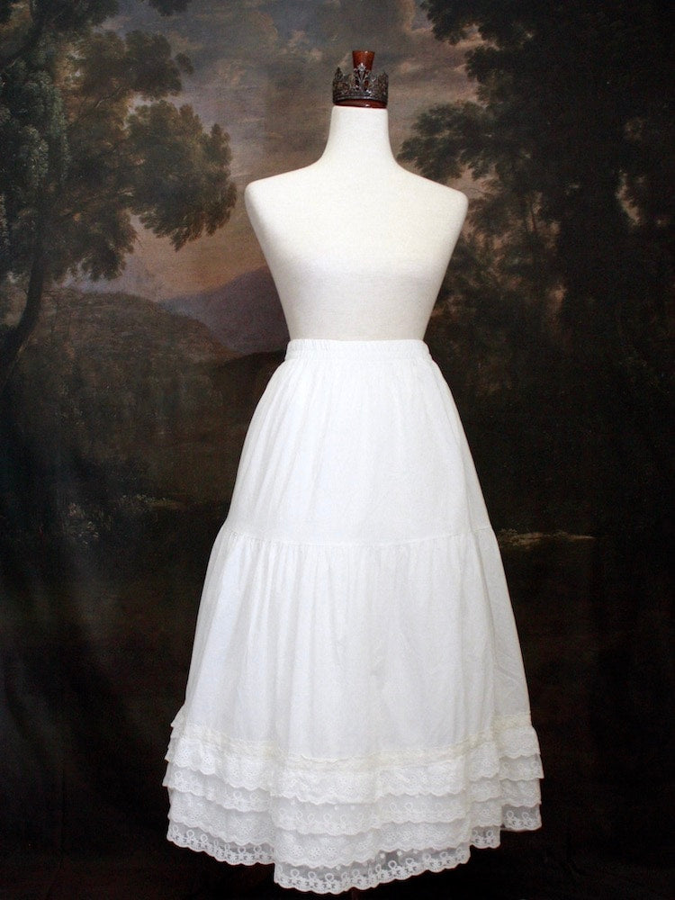 A Historically Inspired bohemian Tiered Cotton Maxi Skirt with floral Lace Trim in White on a mannequin in front of an art history backdrop.