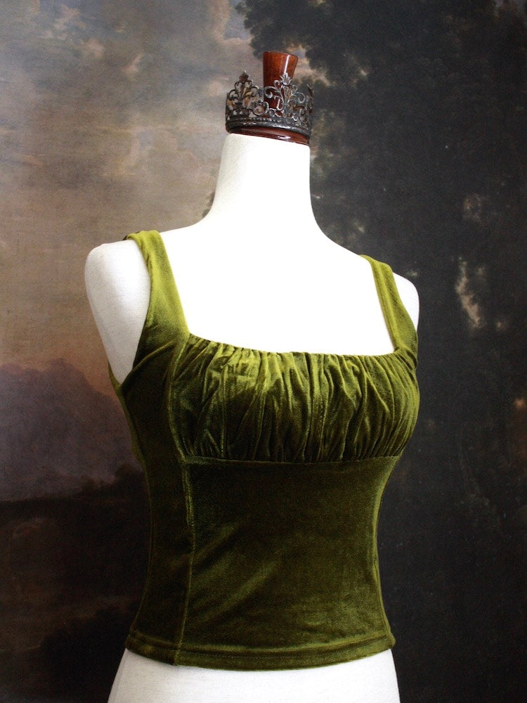 A Historically Inspired medieval fantasy Velvet Milkmaid Bustier Top in Moss Green in front of a historical painting backdrop of a forest.