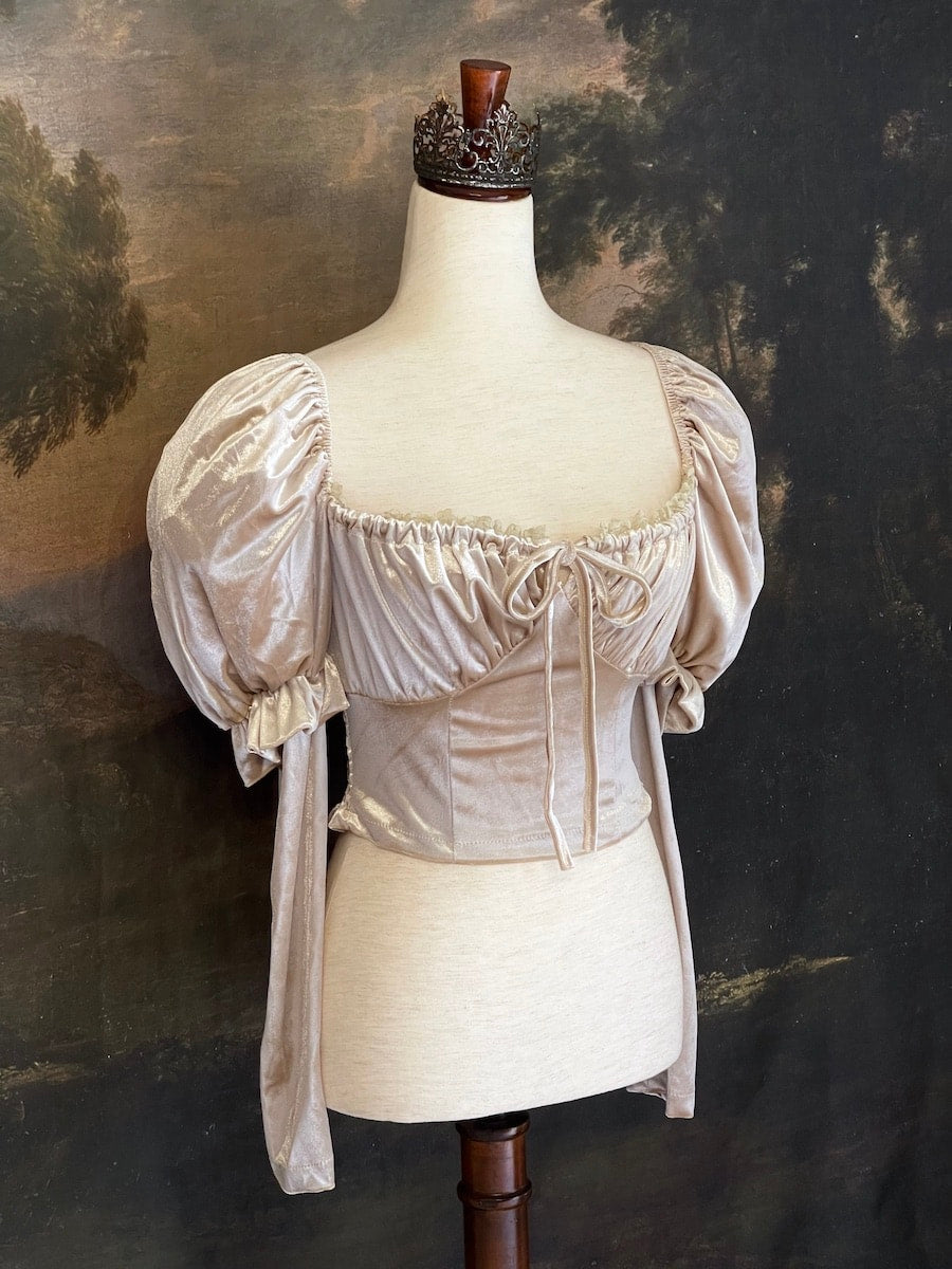 A historically Inspired champagne colored renaissance milkmaid blouse with gigot sleeves is pictured on a mannequin in front of a historical landscape painting Wallpaper.