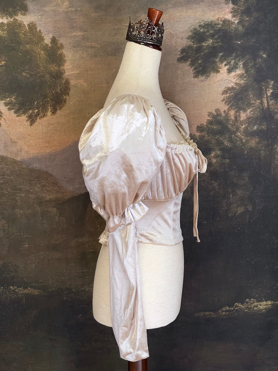 A historically Inspired champagne colored renaissance milkmaid blouse with gigot sleeves is pictured on a mannequin in front of a historical landscape painting Wallpaper.