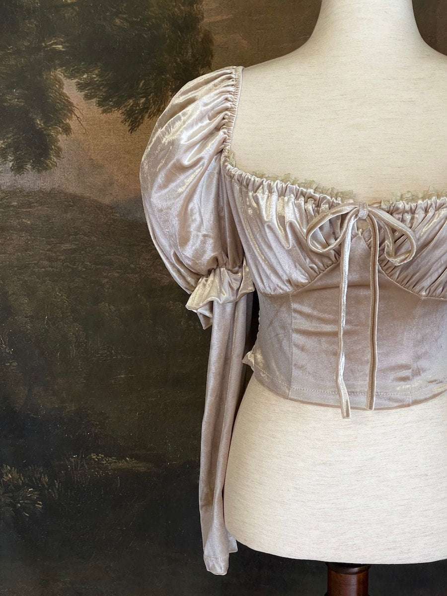 A historically Inspired champagne colored renaissance milkmaid blouse with gigot sleeves is pictured on a mannequin in front of a historical landscape painting Wallpaper.