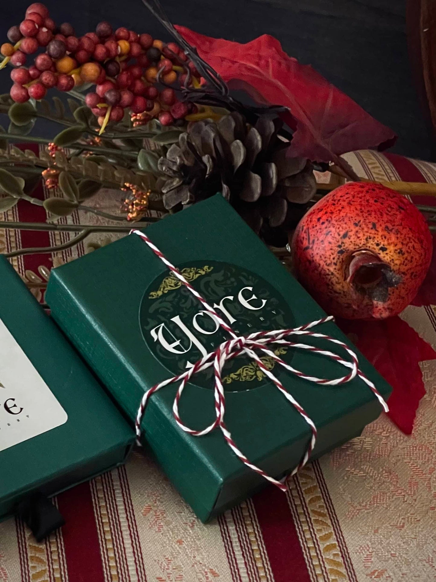 A green, red, and white holiday gift box for historical jewelry with the Yore Logo and a red and white candy-striped bow.