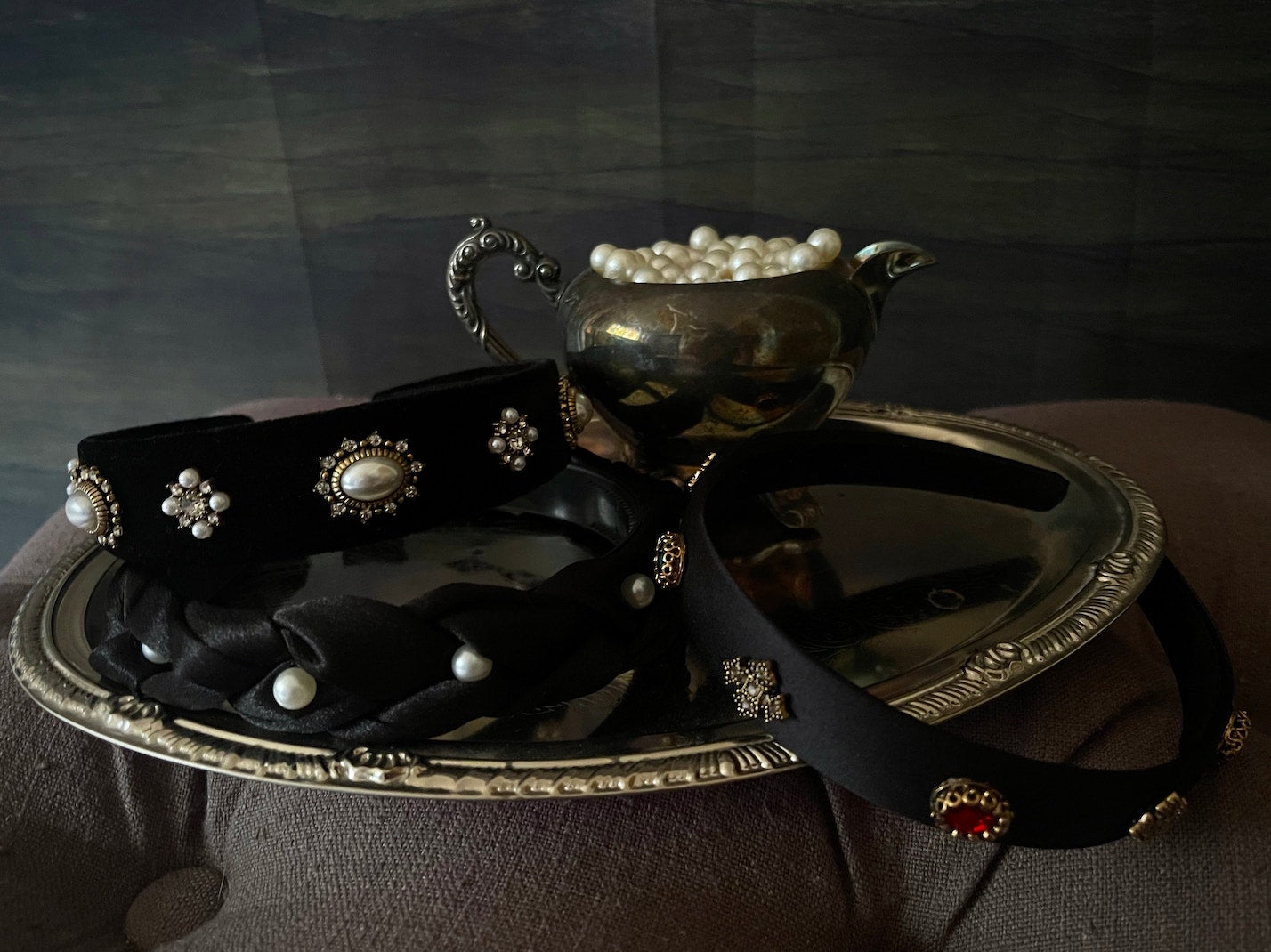 Several medieval and renaissance inspired jewelled headbands in satin and velvet displayed on an antique tray.