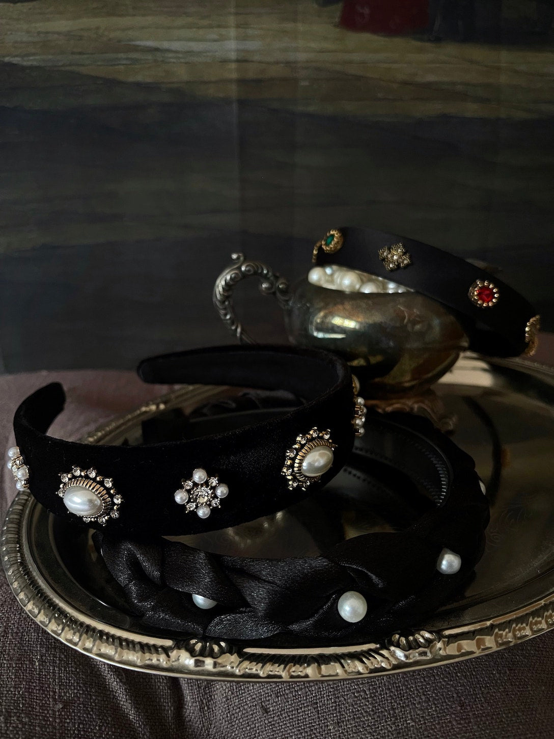 Several medieval and renaissance inspired jewelled headbands in satin and velvet displayed on an antique tray.