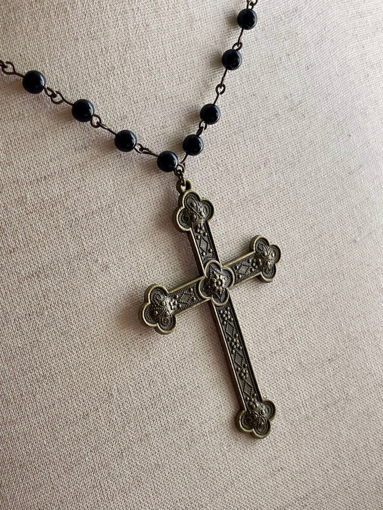 A historically inspired black beaded necklace with a bronze gothic medieval cross pendant is pictured on a mannequin.