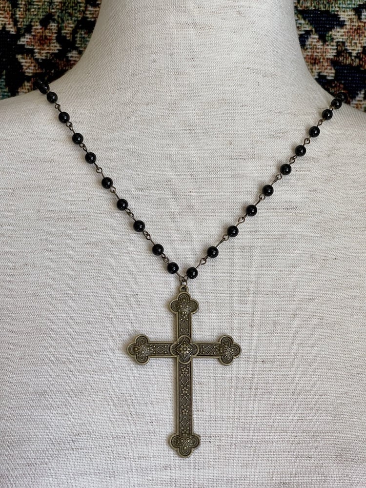 A historically inspired black beaded necklace with a bronze gothic medieval cross pendant is pictured on a mannequin.